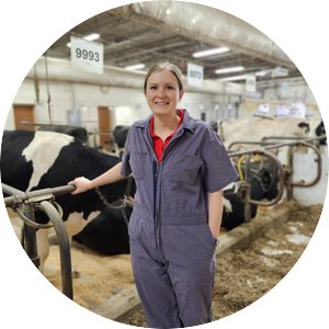 MaryGrace Erickson wearing blue coveralls and standing in front of cows.