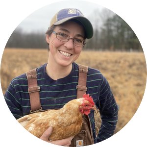 Elizabeth Brownlee wearing overalls and holding a chicken, standing in an open field.