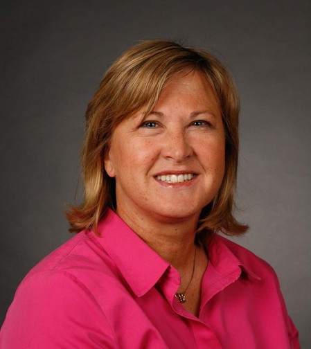 Headshot of Beth Nelson wearing a pink polo shirt and posed in-front of a grey backdrop.