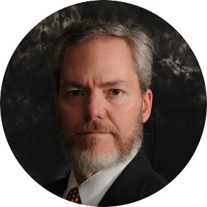 John Chapman is a white man with gray hair parted on the side, wearing a black suit and tie.