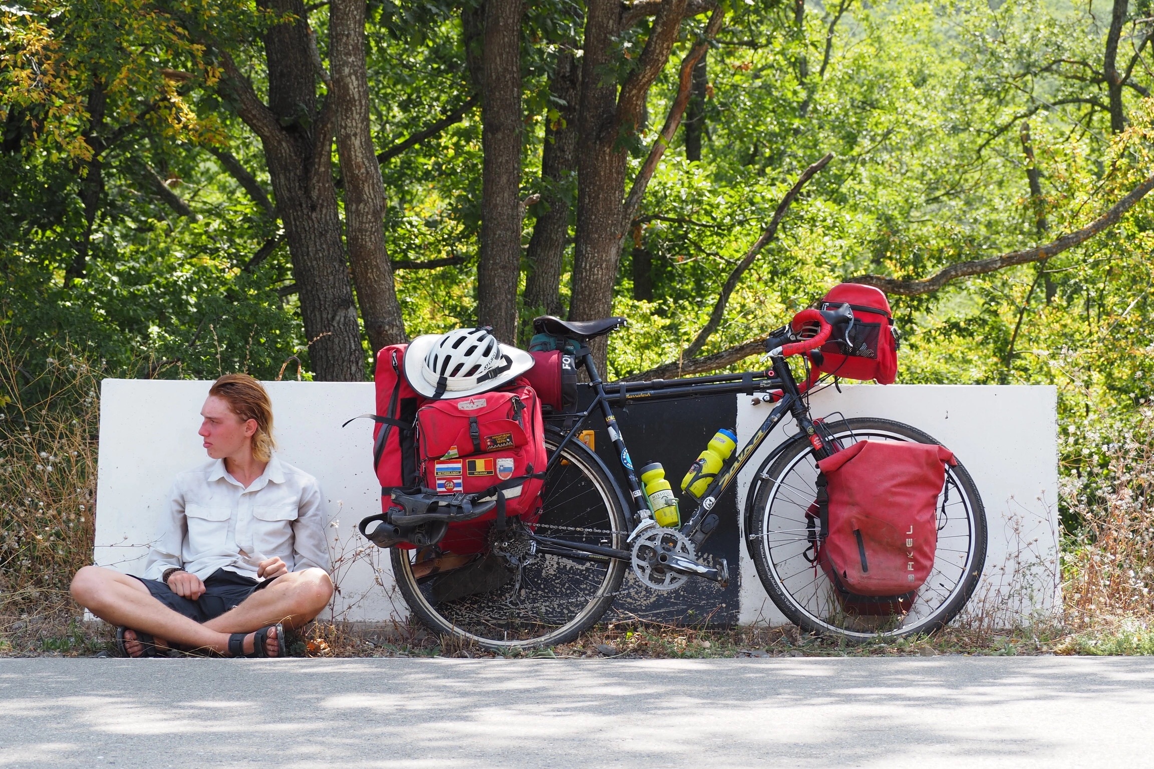 Adam resting roadside next to his bike with trees in the background