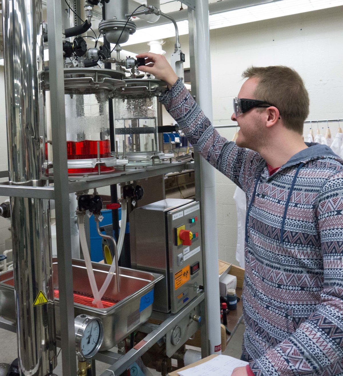 A student makes adjustments to an evaporator machine with clear red liquid in it.