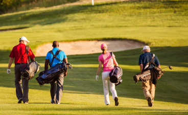 Four golfers walking on a golf course with bright green grass