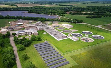 An aerial view looking down on the St. Cloud Wastewater Treatment Plant showing solar panels, green grass, and the treatment facility with reservoir pools full of water. 