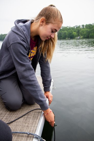 Fayth Nystel holds a water quality sonde in a lake to collect nutrient and chemical data from the lake.