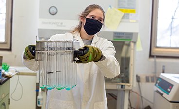 BBE student, Anna Warmka, carries hot test tubes full of bright green samples toward an exhaust vent. 