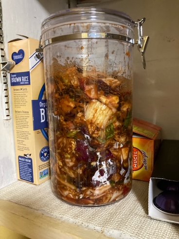 Kimchi fermenting inside a tall glass jar with a metal lid