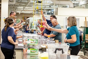 Group of teachers standing around a long table inside a science lab working on experiments