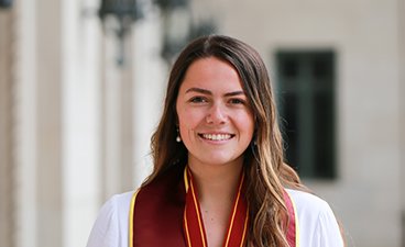 Sarah Whiteside has long brown hair and is wearing a white top with black embroidery with a maroon U of M honors stole for graduation.
