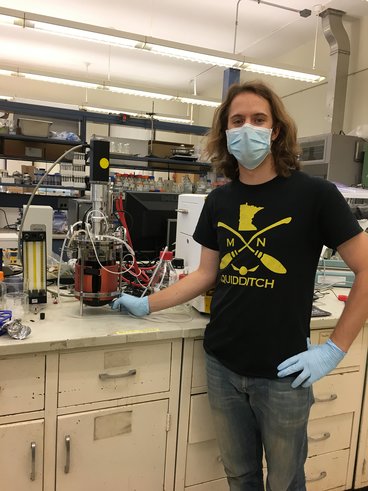 Leif van Lierop stands in a lab wearing a surgical mask and gloves wearing a black tee shirt.