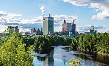 A wide shot of the Sappi paper mill in Cloquet Minnesota, nestled along the St. Louis River surrounded by trees.