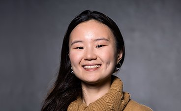 Rui Cheng poses for a professional headshot, she has long black hair and wears a knitted gold turtleneck sweater.