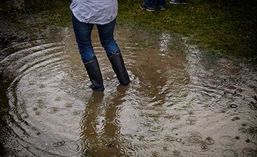 A person stands in ankle deep stormwater wearing rain boots.