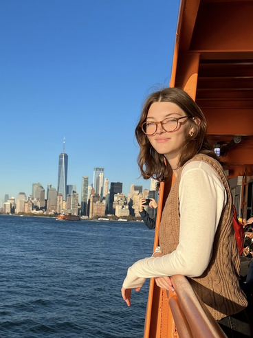 Rhiannon Wilson is leaning over a railing on a ferry outside of Manhattan.